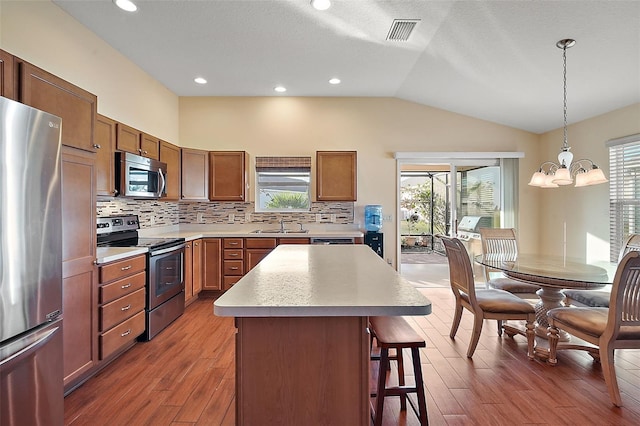 kitchen with stainless steel appliances, a chandelier, pendant lighting, lofted ceiling, and a kitchen island