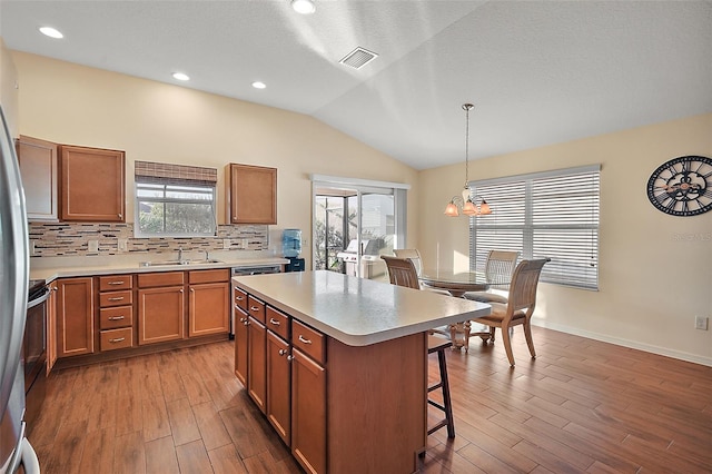 kitchen with sink, hardwood / wood-style floors, pendant lighting, vaulted ceiling, and a kitchen island