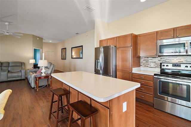 kitchen featuring ceiling fan, a center island, a kitchen breakfast bar, tasteful backsplash, and appliances with stainless steel finishes