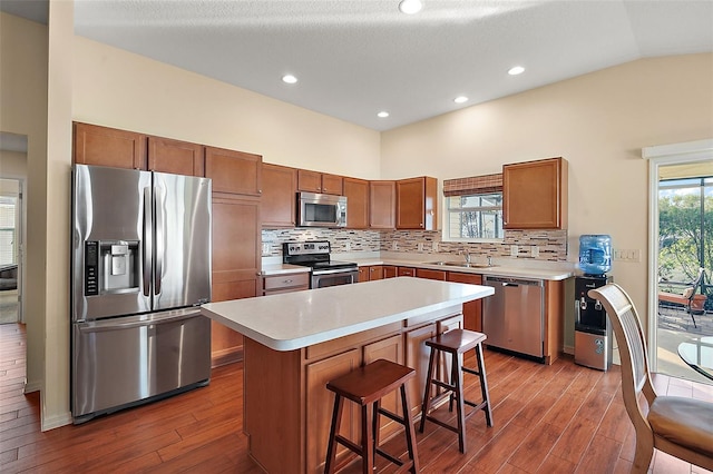 kitchen with sink, stainless steel appliances, vaulted ceiling, a breakfast bar, and a kitchen island