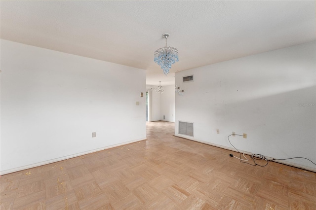 spare room featuring light parquet flooring and an inviting chandelier