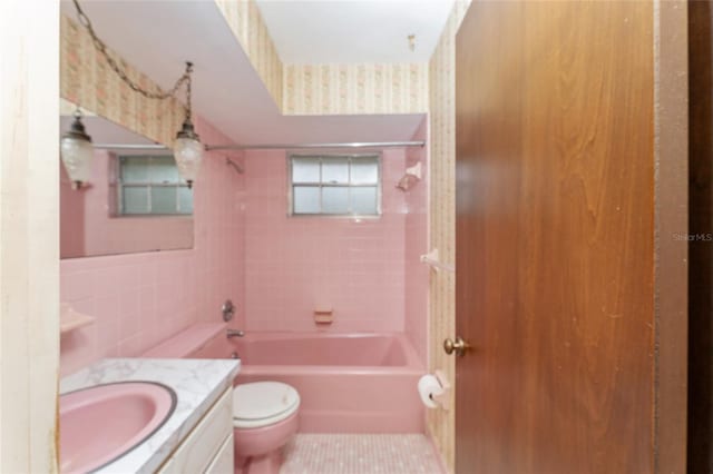 full bathroom with vanity, tile patterned floors, tiled shower / bath, toilet, and tile walls