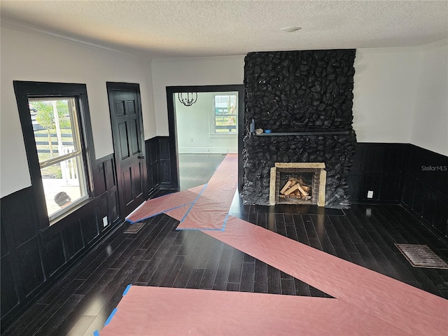 foyer entrance with a stone fireplace, ornamental molding, a textured ceiling, and dark wood-type flooring