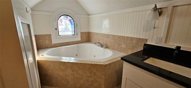 bathroom featuring a textured ceiling, vanity, vaulted ceiling, and tiled tub