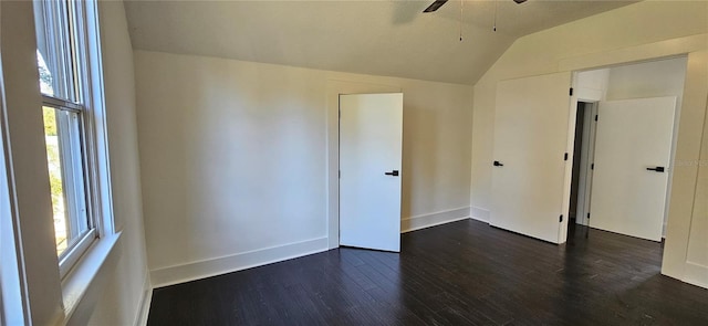 empty room with a healthy amount of sunlight, ceiling fan, dark hardwood / wood-style floors, and vaulted ceiling