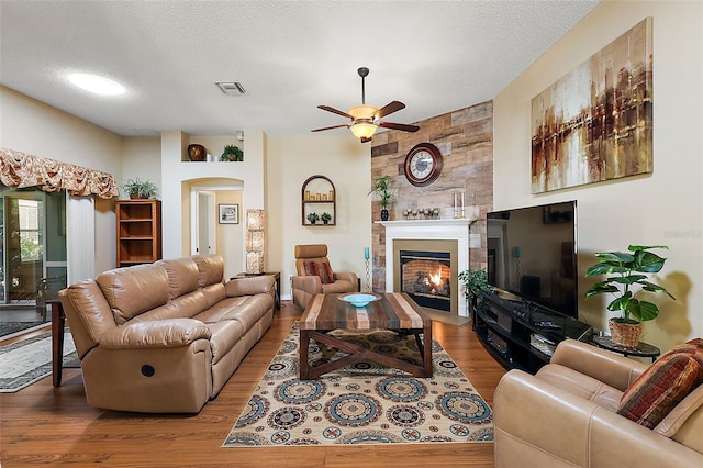 living room featuring light wood-type flooring, a textured ceiling, ceiling fan, and a large fireplace