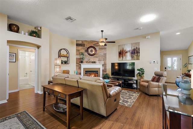 living room with ceiling fan, hardwood / wood-style floors, a textured ceiling, and a large fireplace