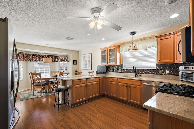 kitchen with appliances with stainless steel finishes, hanging light fixtures, sink, kitchen peninsula, and a breakfast bar