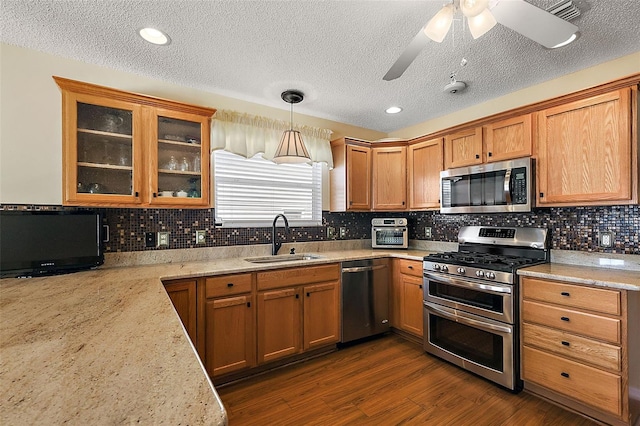 kitchen with appliances with stainless steel finishes, hanging light fixtures, sink, ceiling fan, and light stone counters