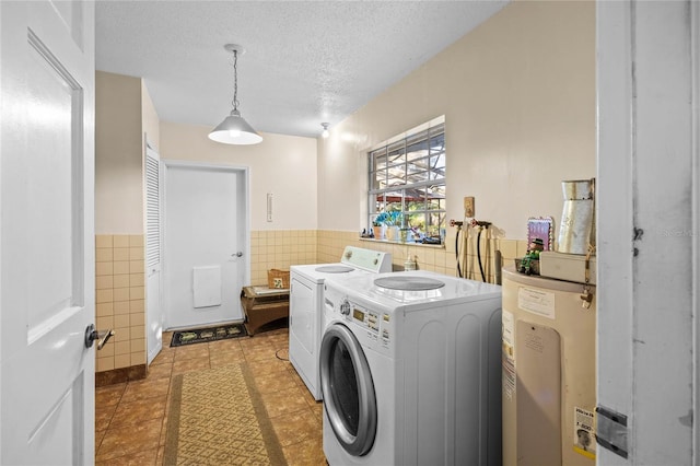 laundry room featuring washing machine and clothes dryer, water heater, dark tile patterned floors, a textured ceiling, and tile walls