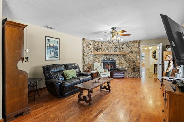 living room featuring a stone fireplace, ceiling fan, a textured ceiling, and hardwood / wood-style flooring