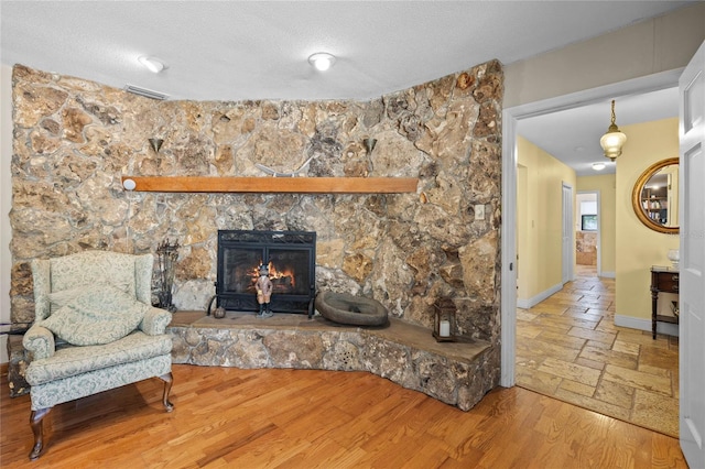 living room with a textured ceiling, hardwood / wood-style flooring, and a stone fireplace