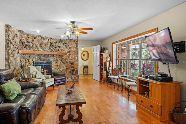 living room with a textured ceiling, light hardwood / wood-style floors, a wood stove, and ceiling fan