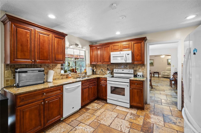 kitchen featuring white appliances, backsplash, sink, ceiling fan, and light stone countertops