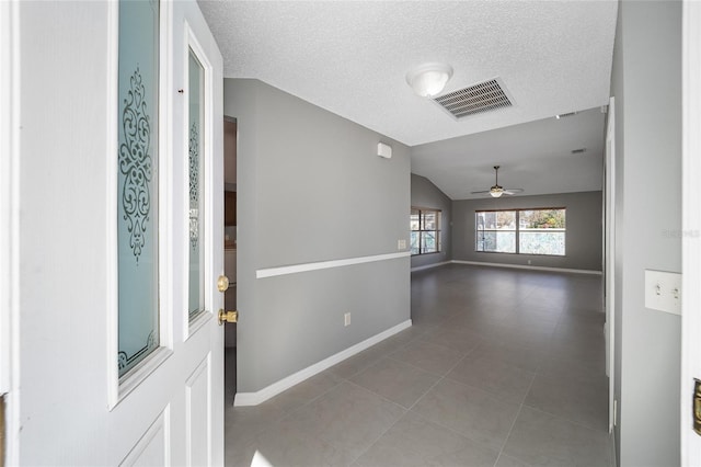 tiled entrance foyer with ceiling fan, vaulted ceiling, and a textured ceiling