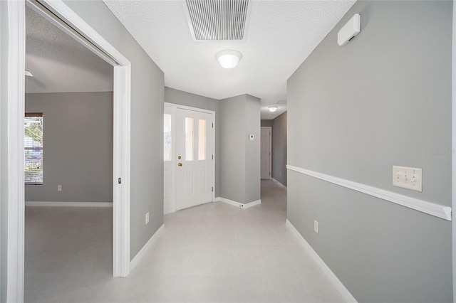 hallway with a textured ceiling and light tile patterned flooring