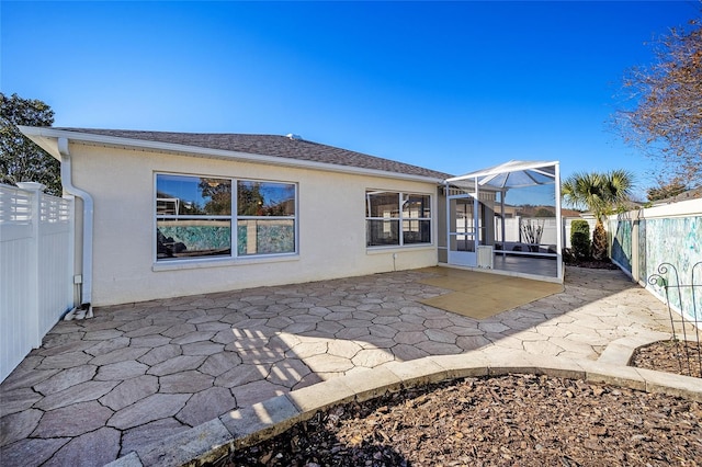 rear view of property featuring glass enclosure and a patio area