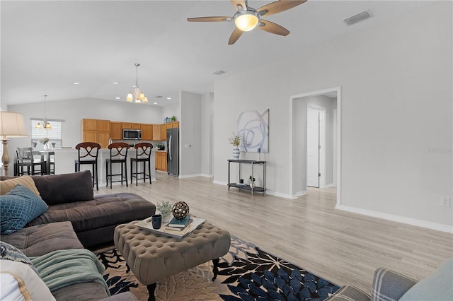 living room with lofted ceiling, ceiling fan with notable chandelier, and light wood-type flooring