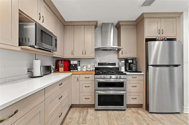 kitchen featuring wall chimney exhaust hood, light brown cabinetry, appliances with stainless steel finishes, and light hardwood / wood-style flooring