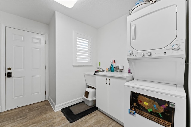 laundry room featuring cabinets, light hardwood / wood-style flooring, and stacked washer / drying machine