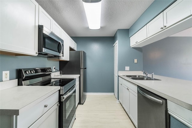 kitchen featuring light wood-type flooring, a textured ceiling, stainless steel appliances, sink, and white cabinets