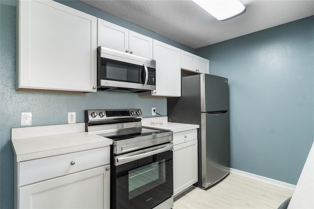 kitchen with white cabinets, stainless steel appliances, a textured ceiling, and light wood-type flooring