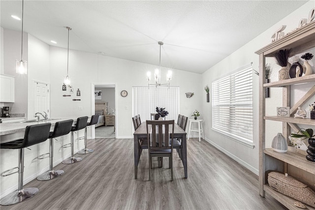 dining room featuring a textured ceiling, a chandelier, light hardwood / wood-style flooring, and vaulted ceiling