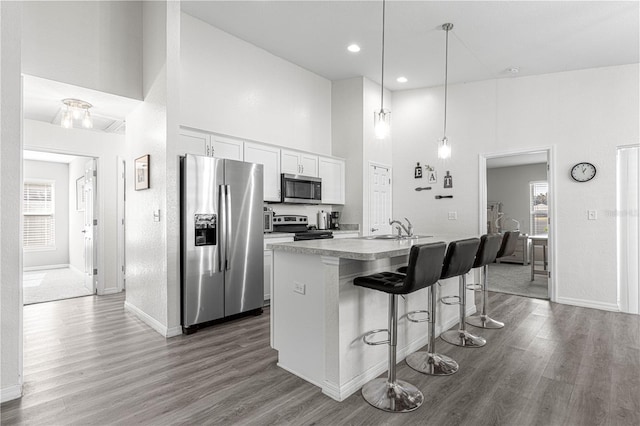 kitchen featuring a kitchen island with sink, a high ceiling, decorative light fixtures, white cabinetry, and stainless steel appliances