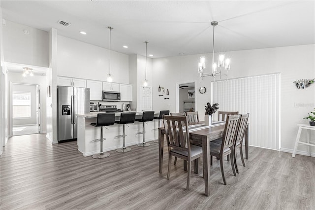 dining space with light wood-type flooring, a towering ceiling, and a chandelier