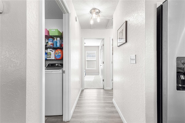 corridor with crown molding, light hardwood / wood-style flooring, a textured ceiling, and washer / dryer