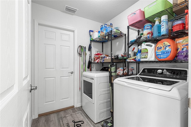 clothes washing area with a textured ceiling, washing machine and dryer, and light hardwood / wood-style floors