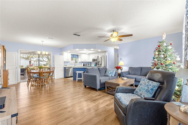 living room with light wood-type flooring, a textured ceiling, and ceiling fan with notable chandelier