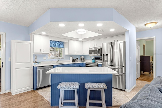 kitchen with a textured ceiling, stainless steel appliances, sink, a center island, and white cabinetry