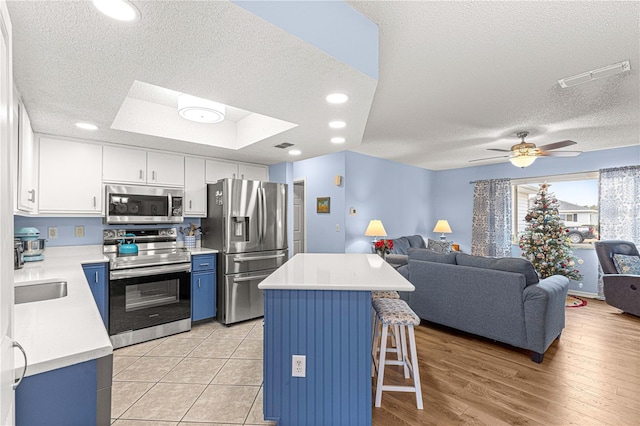 kitchen with appliances with stainless steel finishes, a kitchen breakfast bar, a raised ceiling, white cabinets, and a kitchen island