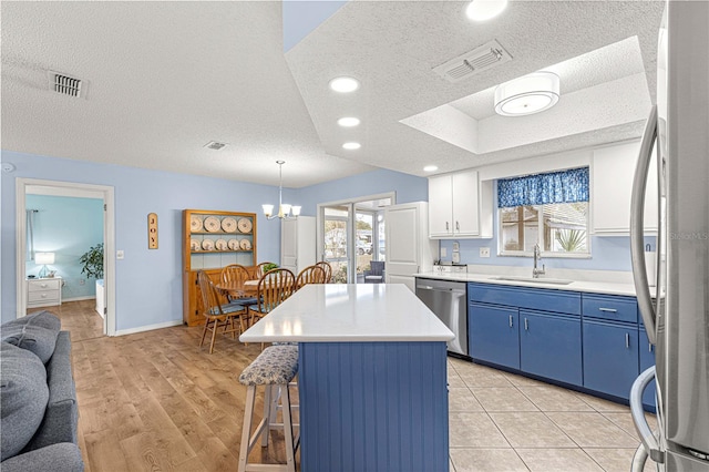 kitchen with appliances with stainless steel finishes, sink, pendant lighting, a center island, and white cabinetry