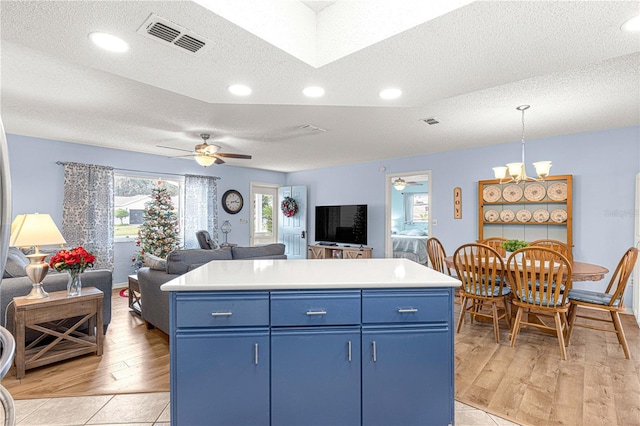 kitchen with a textured ceiling, ceiling fan with notable chandelier, blue cabinets, pendant lighting, and a center island