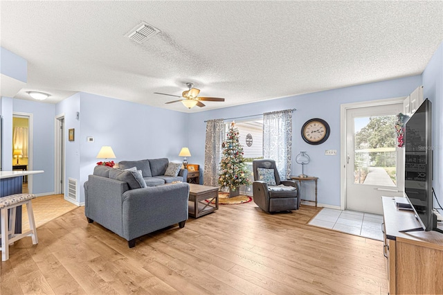 living room featuring a wealth of natural light, ceiling fan, a textured ceiling, and light wood-type flooring