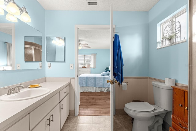 bathroom with ceiling fan, tile patterned flooring, a textured ceiling, toilet, and vanity