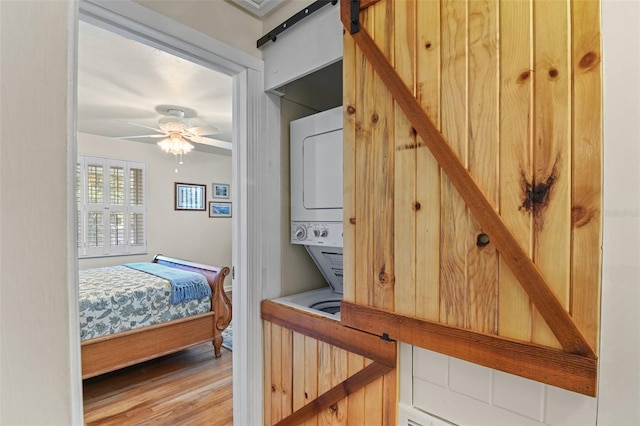 bedroom featuring light wood-type flooring, a barn door, ceiling fan, and stacked washer and clothes dryer