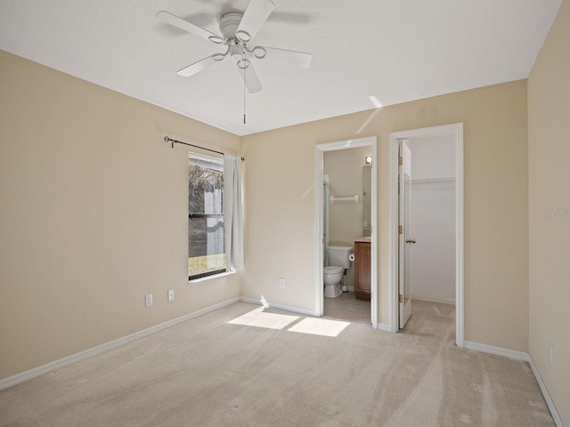 unfurnished bedroom with connected bathroom, a spacious closet, ceiling fan, light colored carpet, and a closet