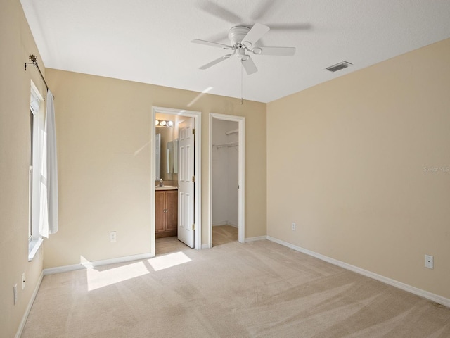 unfurnished bedroom with ensuite bath, ceiling fan, a spacious closet, light colored carpet, and a closet