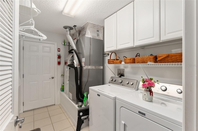 laundry area with washing machine and dryer, light tile patterned floors, cabinets, and a textured ceiling