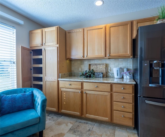 kitchen featuring black fridge, decorative backsplash, a textured ceiling, and light stone countertops