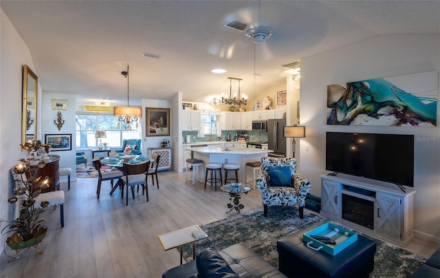 living room featuring a textured ceiling, light hardwood / wood-style flooring, lofted ceiling, and ceiling fan with notable chandelier