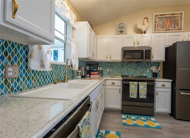 kitchen featuring stainless steel appliances, sink, white cabinetry, lofted ceiling, and tasteful backsplash