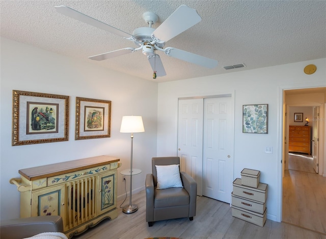 sitting room with light hardwood / wood-style floors, ceiling fan, and a textured ceiling