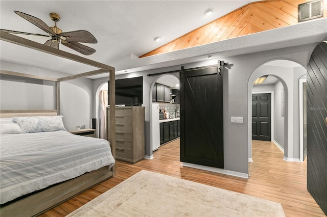 bedroom featuring vaulted ceiling, a barn door, ceiling fan, and light wood-type flooring