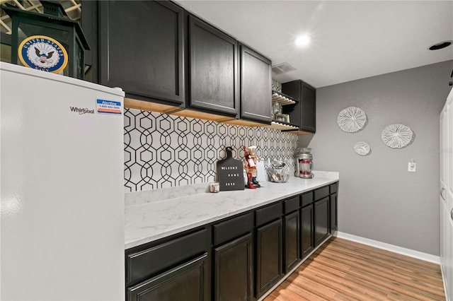 kitchen with tasteful backsplash, light stone counters, light hardwood / wood-style floors, and white fridge