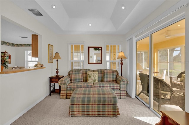 living area with a raised ceiling, a wealth of natural light, and light carpet