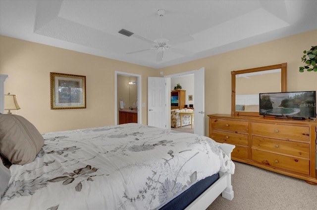 carpeted bedroom with a raised ceiling, ensuite bath, and ceiling fan